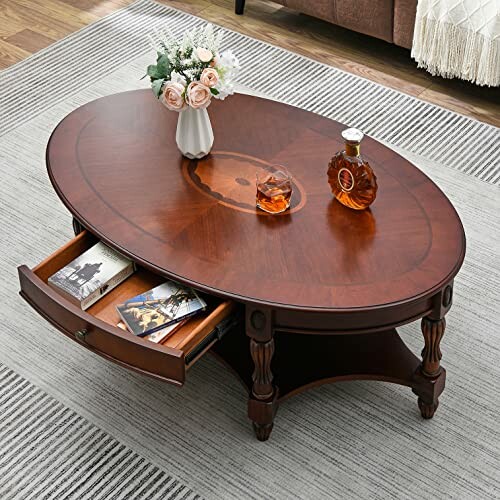 Oval wooden coffee table with a drawer, flowers, and decanter.